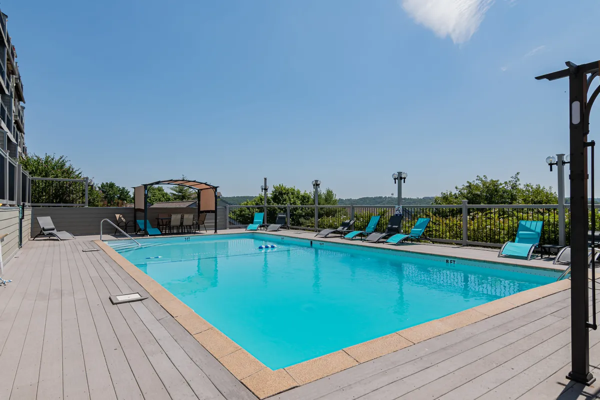 An exterior view of the community pool, complete with lounge chairs and a shaded canopy seating area. The pool is lively, surrounded by lush landscaping and designed for gatherings or relaxing swims. The sunset ambiance hints at the area being well-used into the evening.