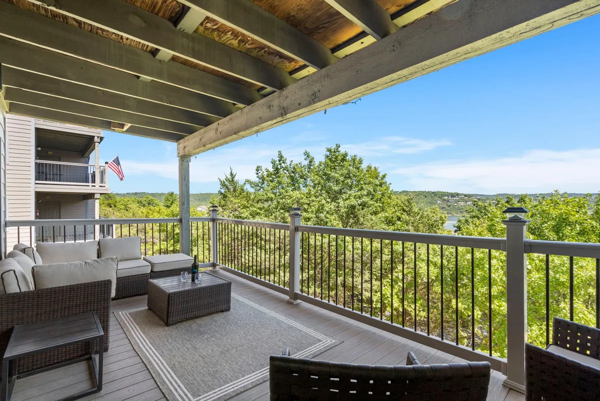 A comfortable deck seating area overlooking lush trees and the surrounding landscape, with a decorative rug and space for relaxing or enjoying a meal outdoors. The view hints at sunset possibilities and a tranquil connection to nature.
