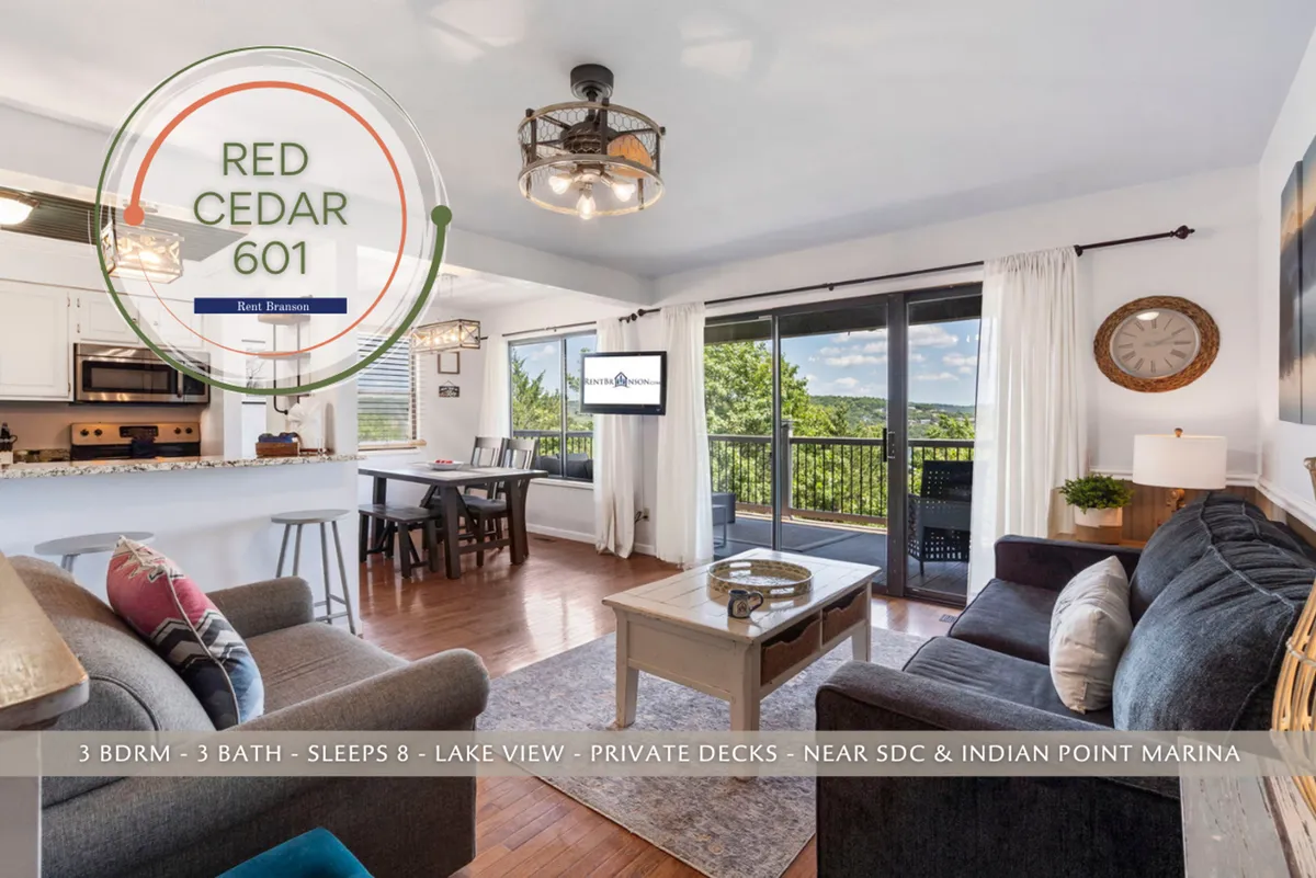 A spacious, open-concept living and dining area, bathed in natural light from large windows that showcase a stunning lake view. There’s a comfortable seating area arranged for socializing or relaxing, a dining table perfect for shared meals or games, and tasteful, inviting decor.