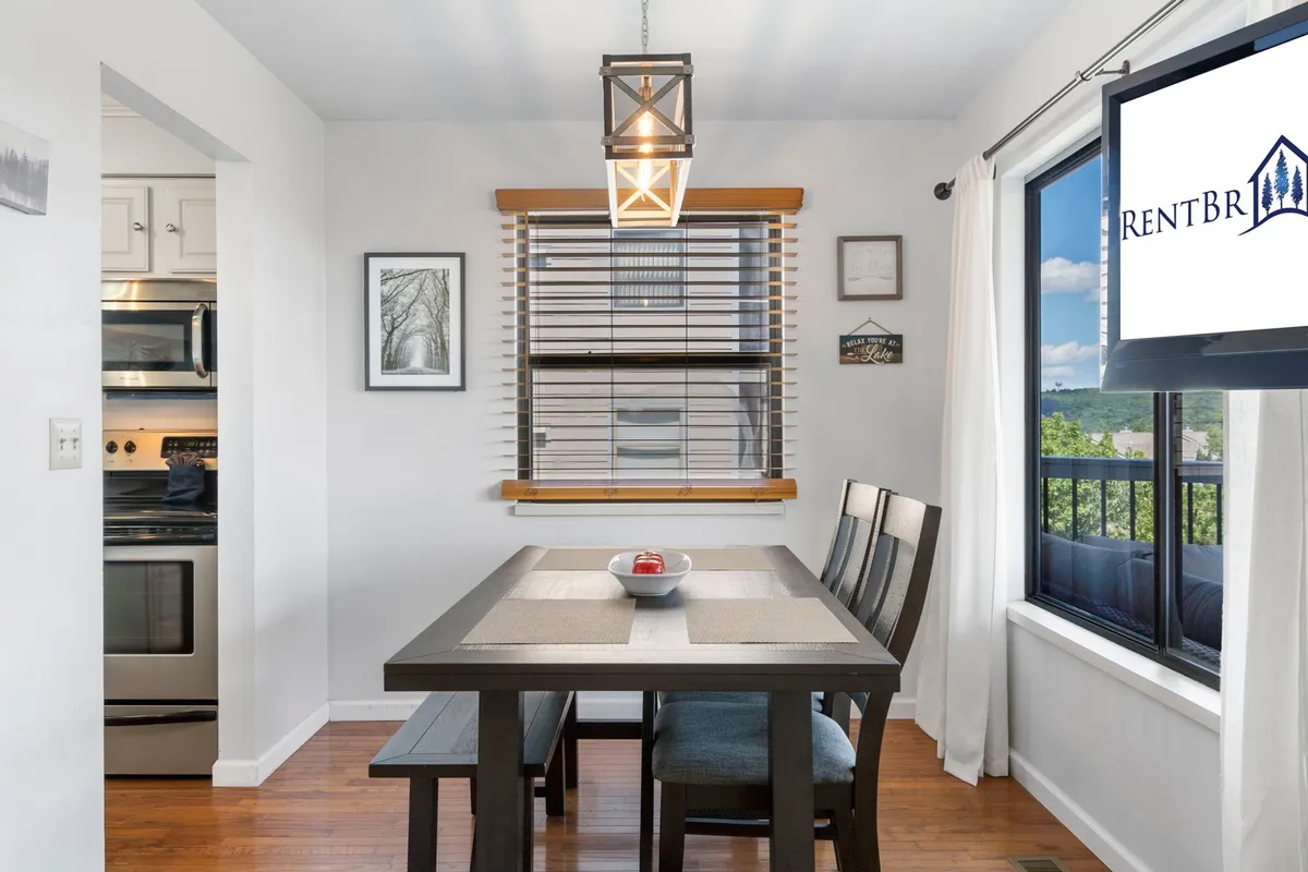 The dining area centers on a table with an attractive centerpiece, set near a window that allows natural light to stream in. Soft, cozy lighting creates an intimate atmosphere, making it ideal for meals or games.
