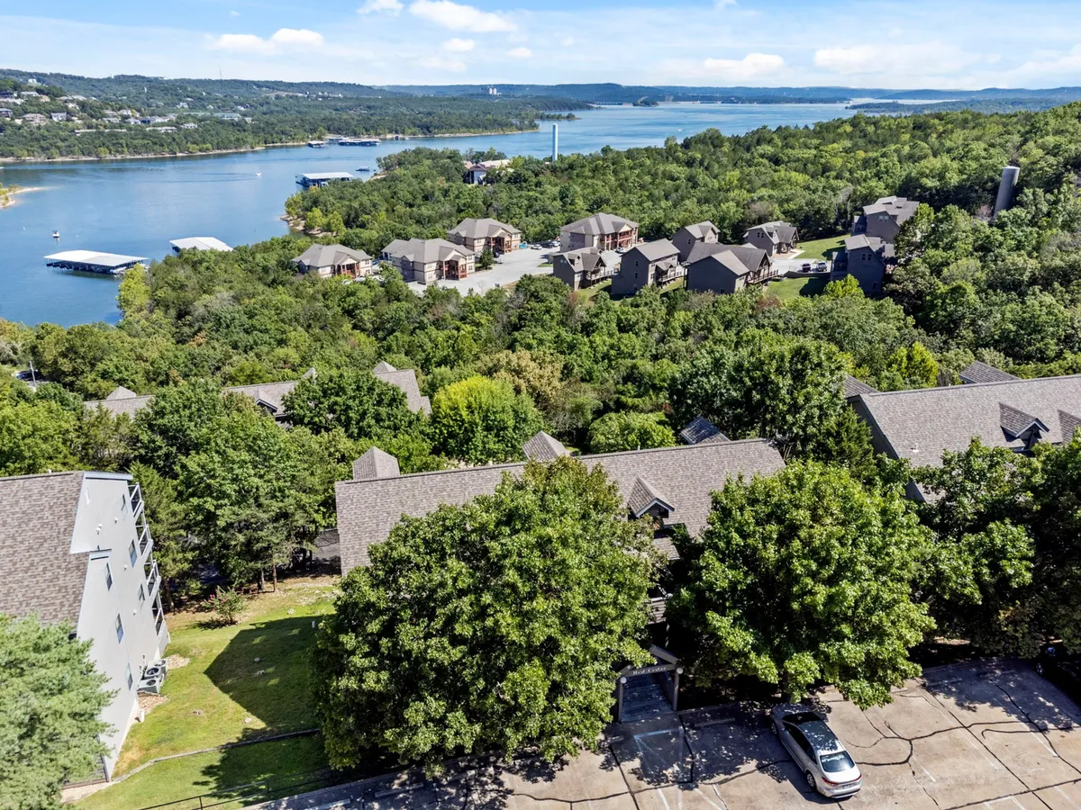 A scenic view of the lake surrounded by lush greenery and residential buildings. The setting is tranquil and ideal for outdoor leisure activities such as boating, hiking, and picnicking. The open water and green landscape capture the essence of Ozarks exploration and lakeside relaxation.