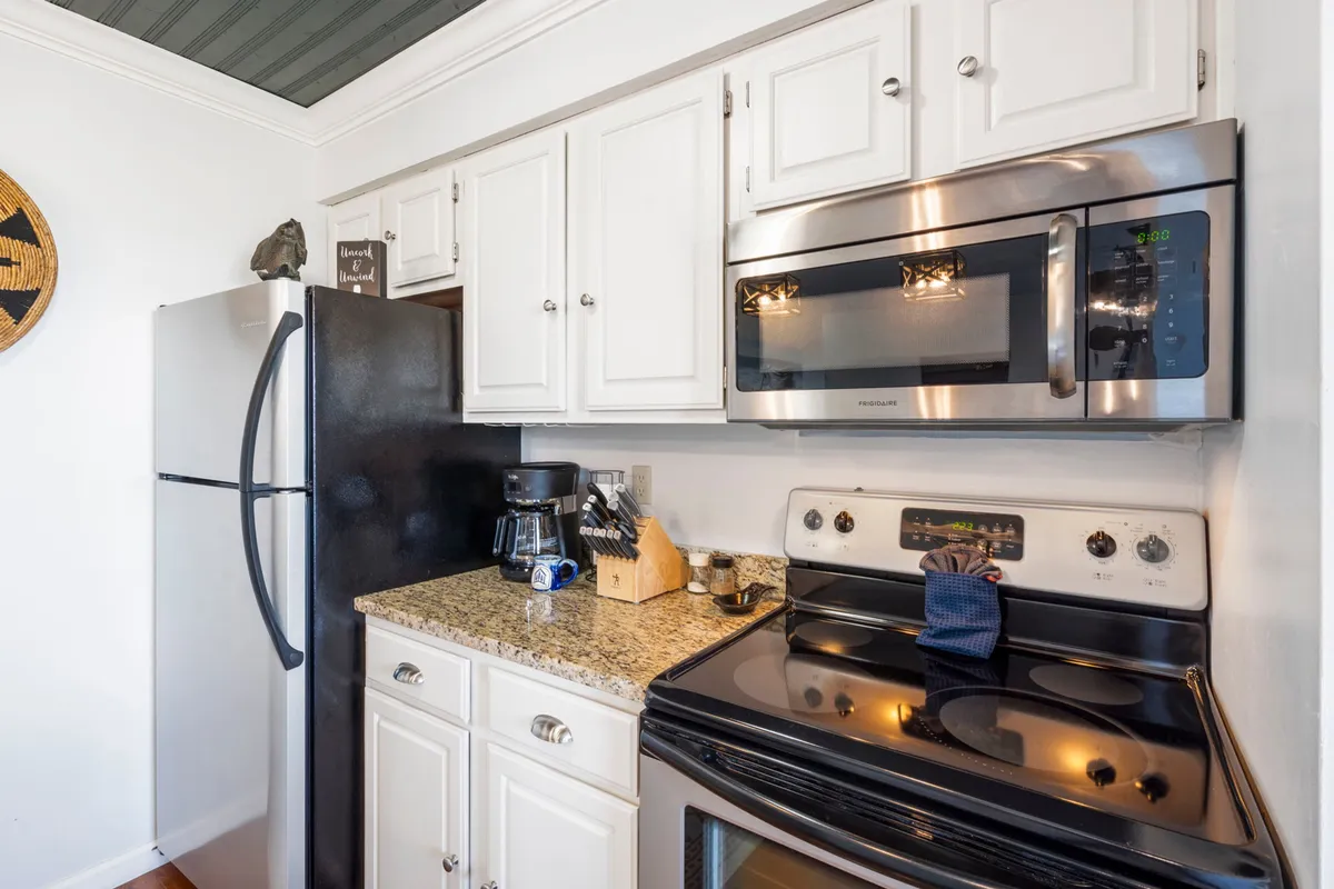 This image features a cozy kitchen space with stainless steel appliances, granite countertops, white cabinets, and various kitchen tools on display. The inviting layout highlights ample prep space and modern amenities, perfect for cooking and gathering.