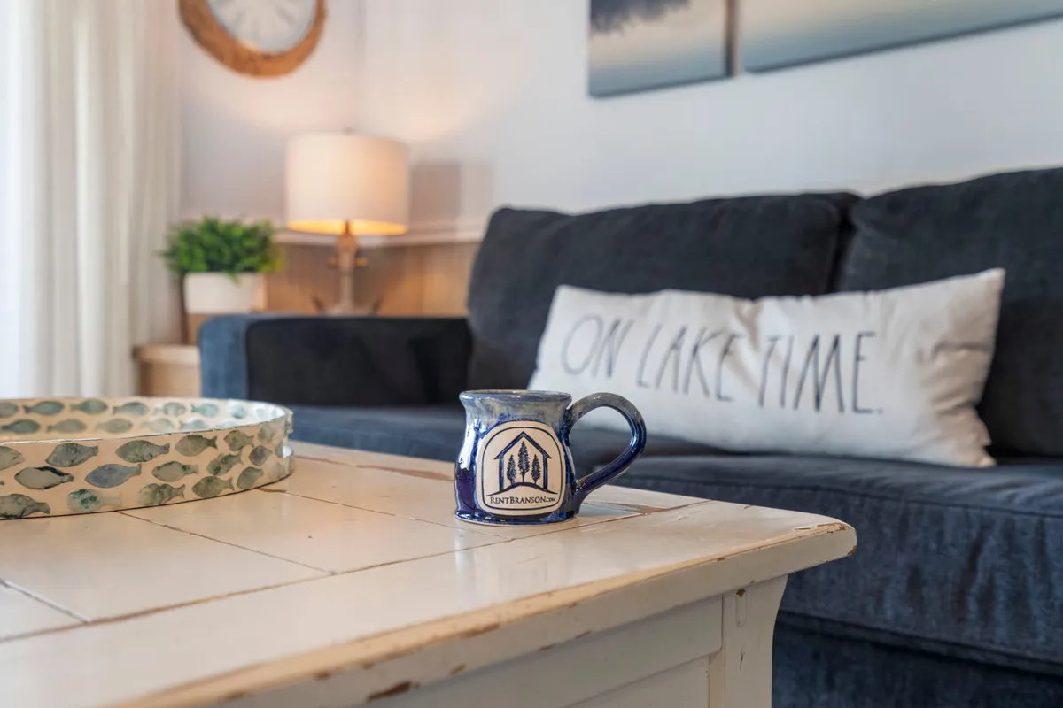 This interior image features a plaid couch with colorful pillows and a blue ceramic mug on a decorative tray, capturing a cozy, laid-back living space ideal for conversation or playing games. The inviting setup suggests a comfortable, family-friendly hangout area, perfect for both kids and adults.