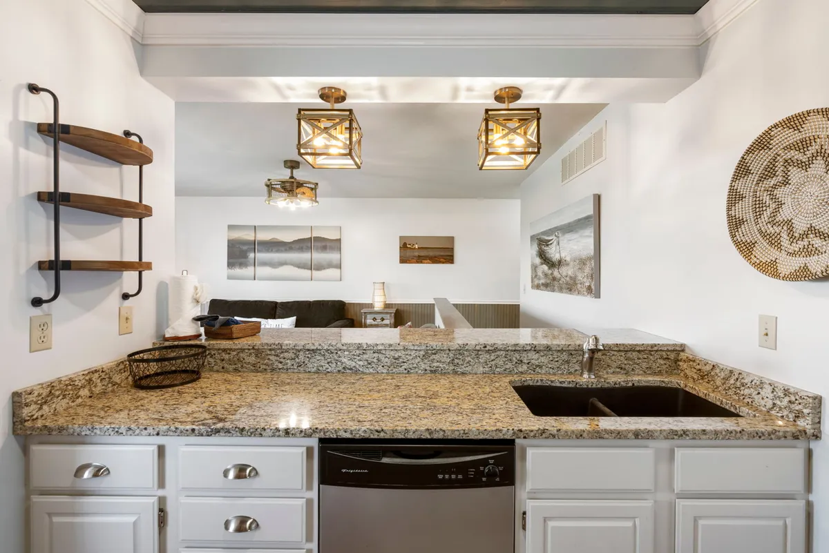 A bright, modern kitchen with granite countertops, stylish lighting, and open sight-lines to the living area. Kitchen appliances and ample counter space suggest a functional, inviting environment for meal preparation and casual dining.