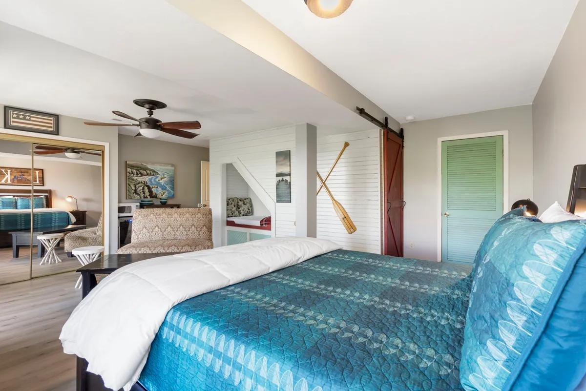 A cozy bedroom with a patterned quilt, wooden accents, decorative paddles on the wall, a sliding barn door, and a mirrored closet. The room is filled with soft light and exudes a sense of warmth and relaxation.