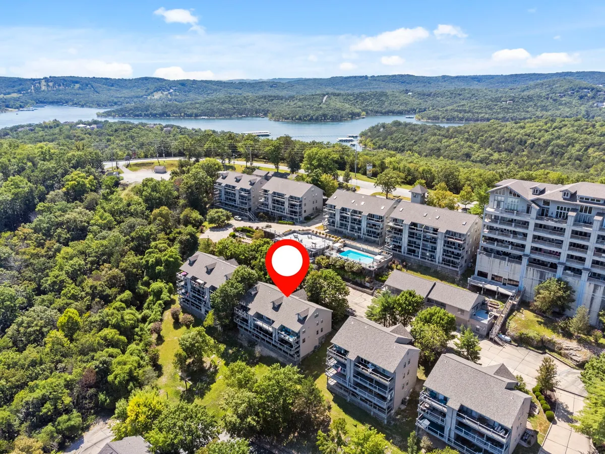 A wide exterior shot featuring the resort’s pool area with lounge chairs, residential buildings, and expansive views of Table Rock Lake and the surrounding forested hills. The scene is tranquil and inviting, with nature and amenities seamlessly blending.